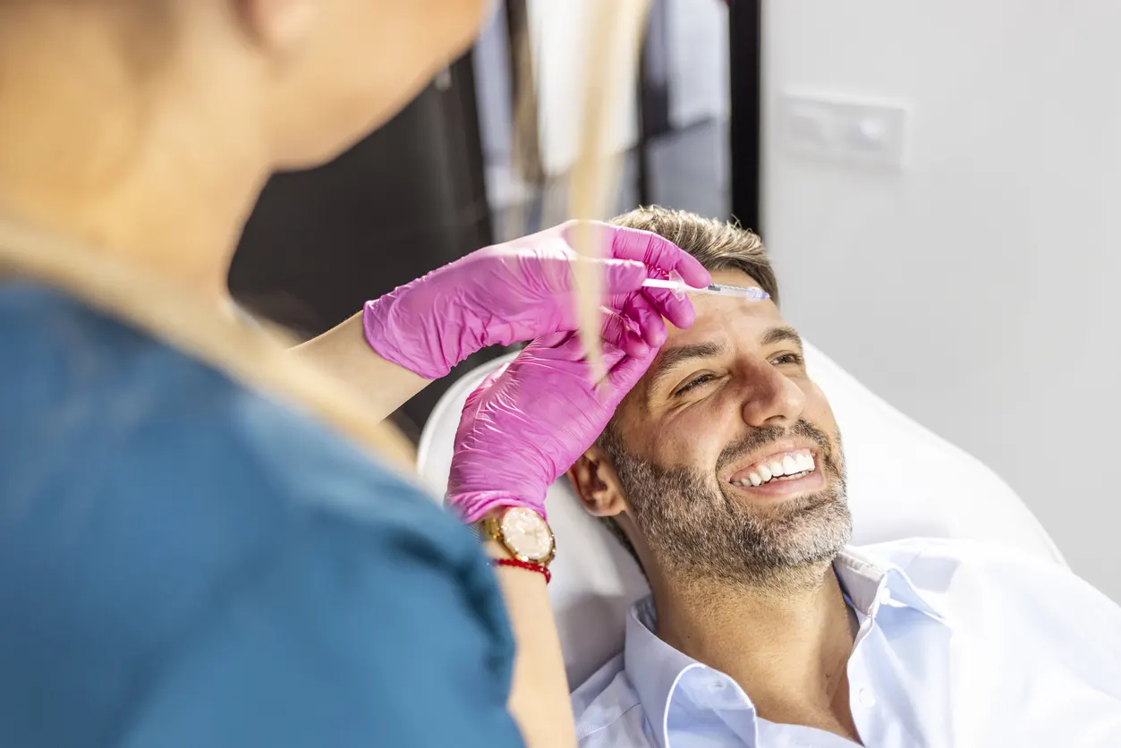 Image of a happy male patient undergoing face filler treatment by beautician